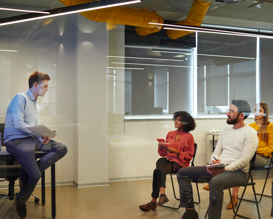 Man sitting on a stool talking to a group of people in a training setting