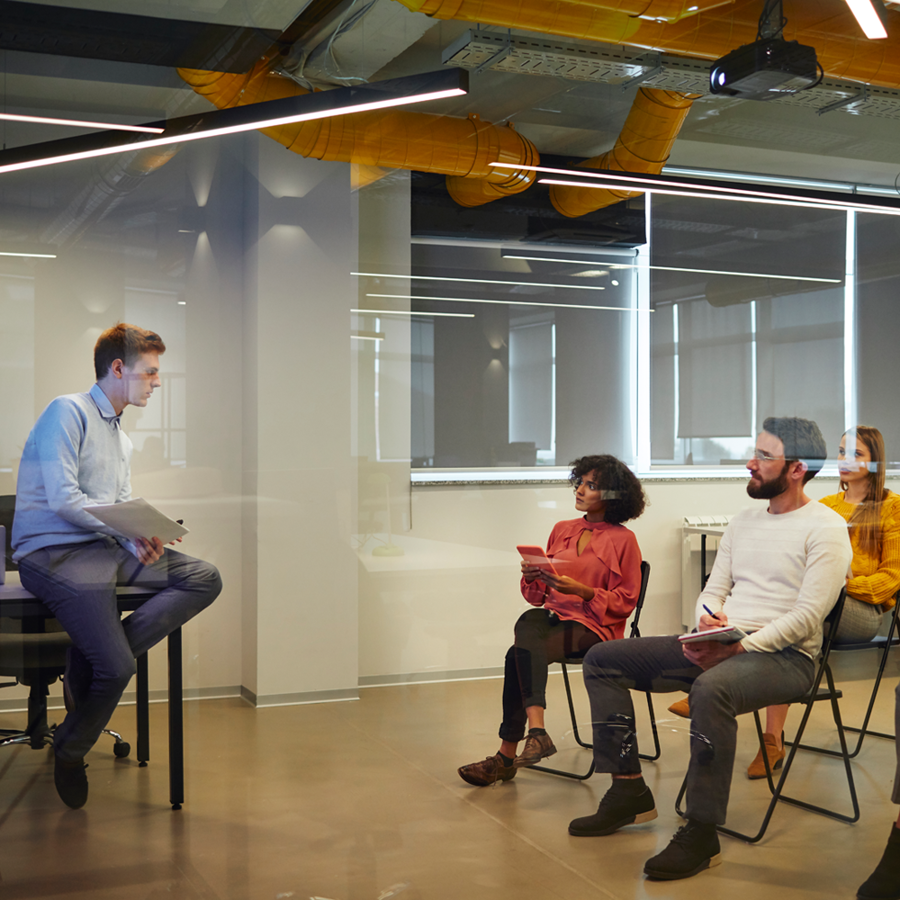 Man sitting on a stool talking to a group of people in a training setting