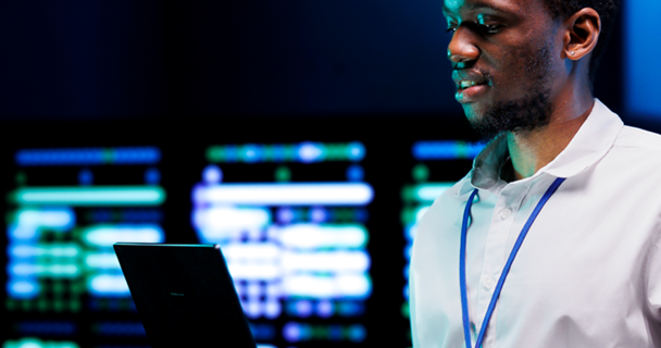 Man standing whilst holding a laptop in an IT setting